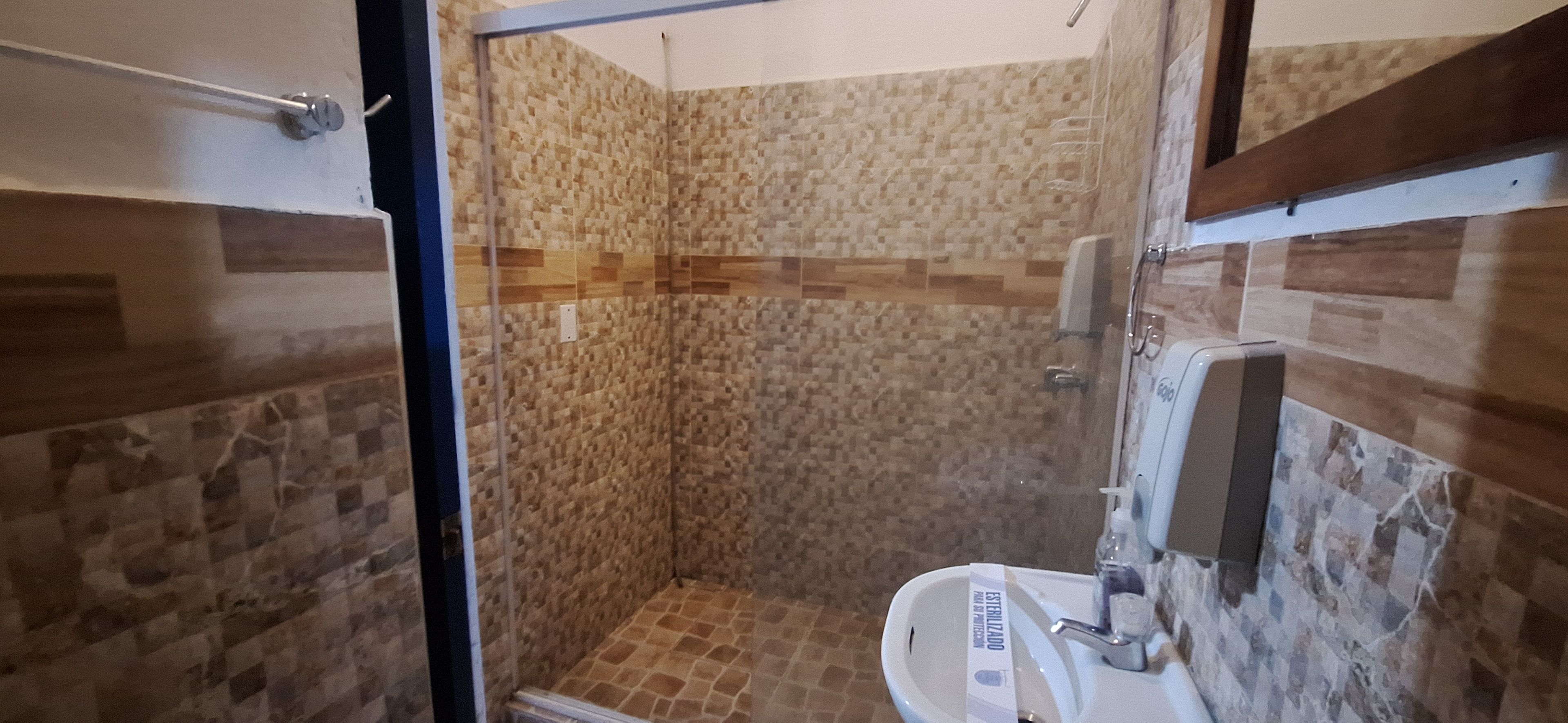 Un petit espace douche fermé, avec des murs carrelés et un lavabo blanc.