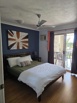Een hotelkamer met een bed, een plafondventilator, een raam met gordijnen en een wandmodel airconditioner.