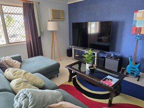 Ein Wohnzimmer mit einer Couch, einem Couchtisch mit einer Zeitschrift, einem Fernseher, einer Gitarre und einer Pflanze.
