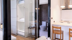 Una camera d'albergo moderna con un separé in vetro, un letto, un tavolino e una sedia.