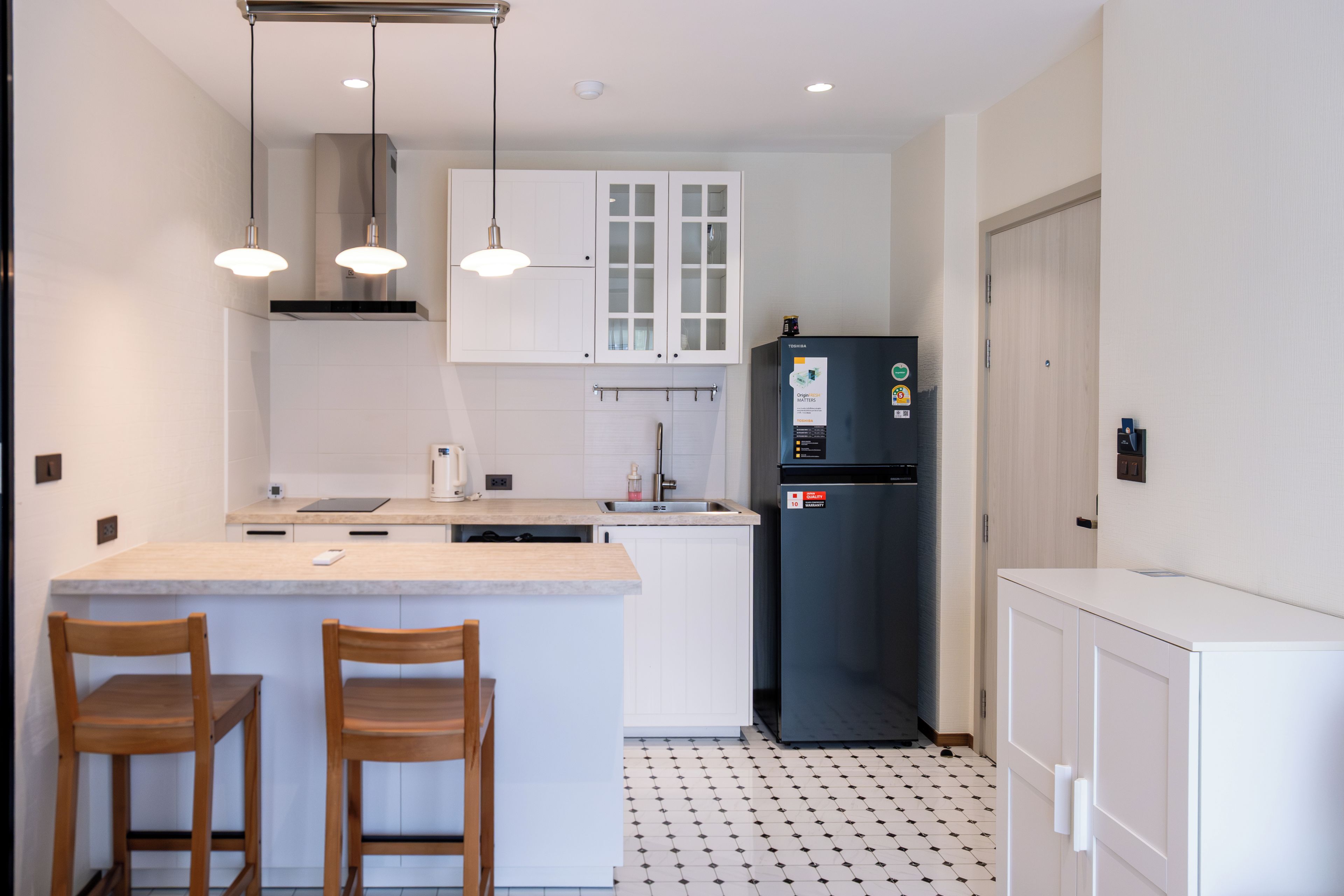 A compact kitchen with a central island, two wooden chairs, a refrigerator, and pendant lighting.