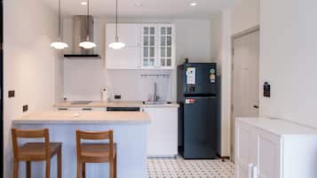 A compact kitchen with a central island, two wooden chairs, a refrigerator, and pendant lighting.