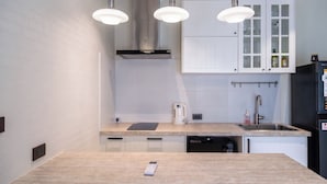 Una cucina moderna con mobili bianchi, una cappa in acciaio inossidabile, illuminazione a sospensione e lavastoviglie integrata.