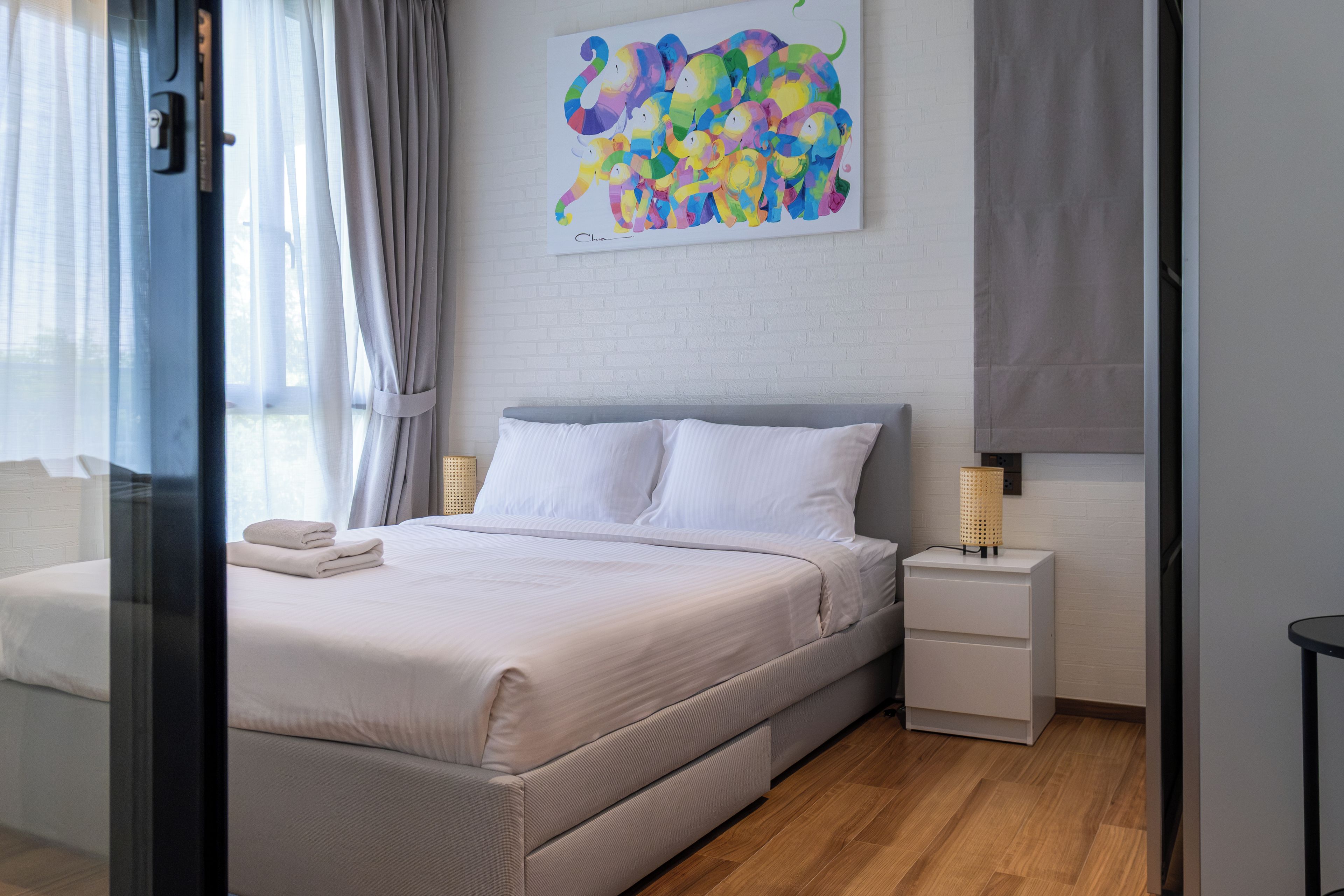A hotel room with a bed, a nightstand, a lamp, and a painting on the wall.
