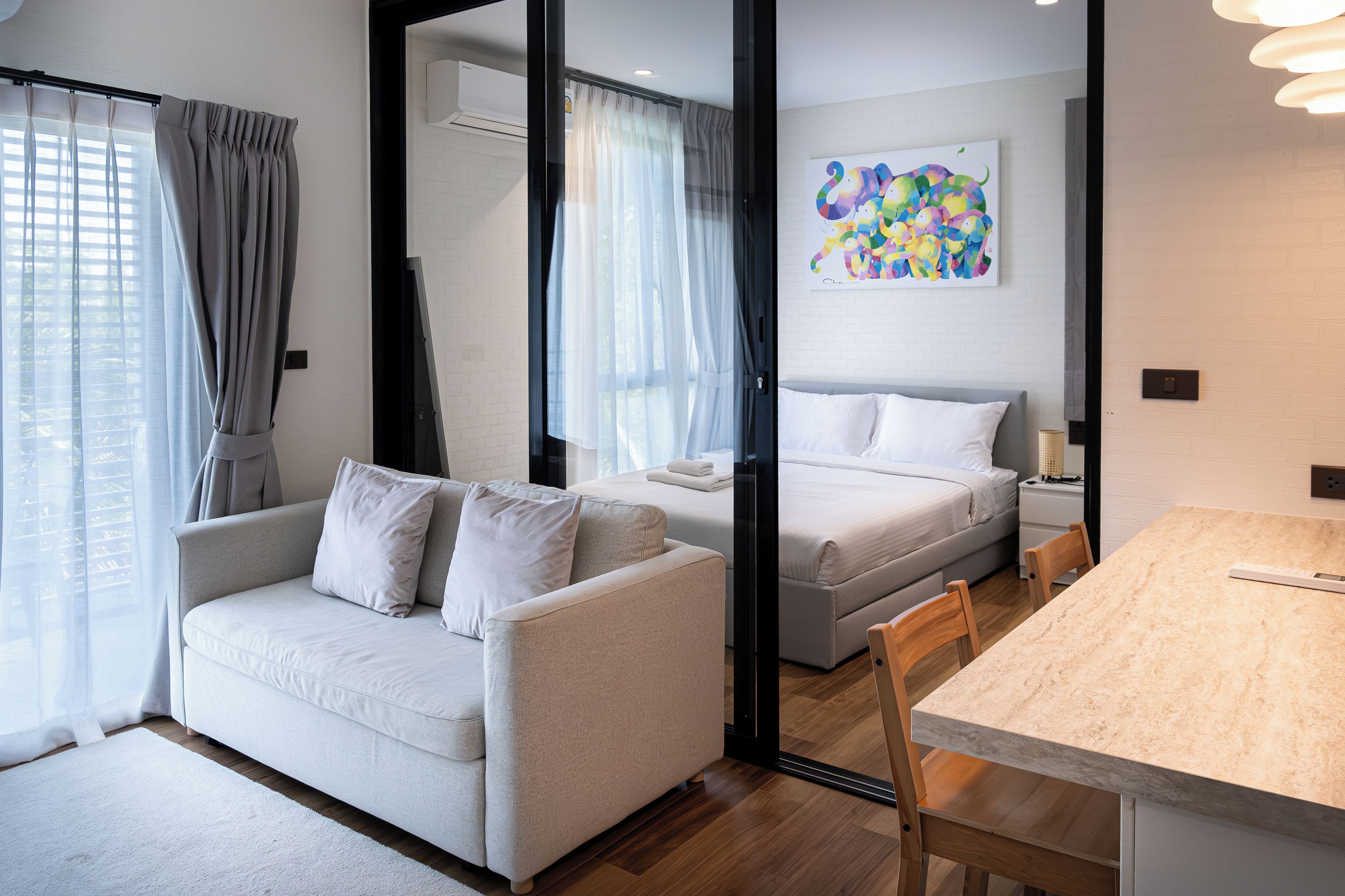 A modern hotel room with a sofa, a bed, a dining table, and a colorful abstract painting on the wall.