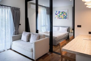 Quarto de hotel moderno com sofá, cama, mesa de jantar e uma pintura abstrata colorida na parede.