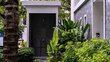 A building entrance with a dark facade, surrounded by lush greenery and a palm tree.