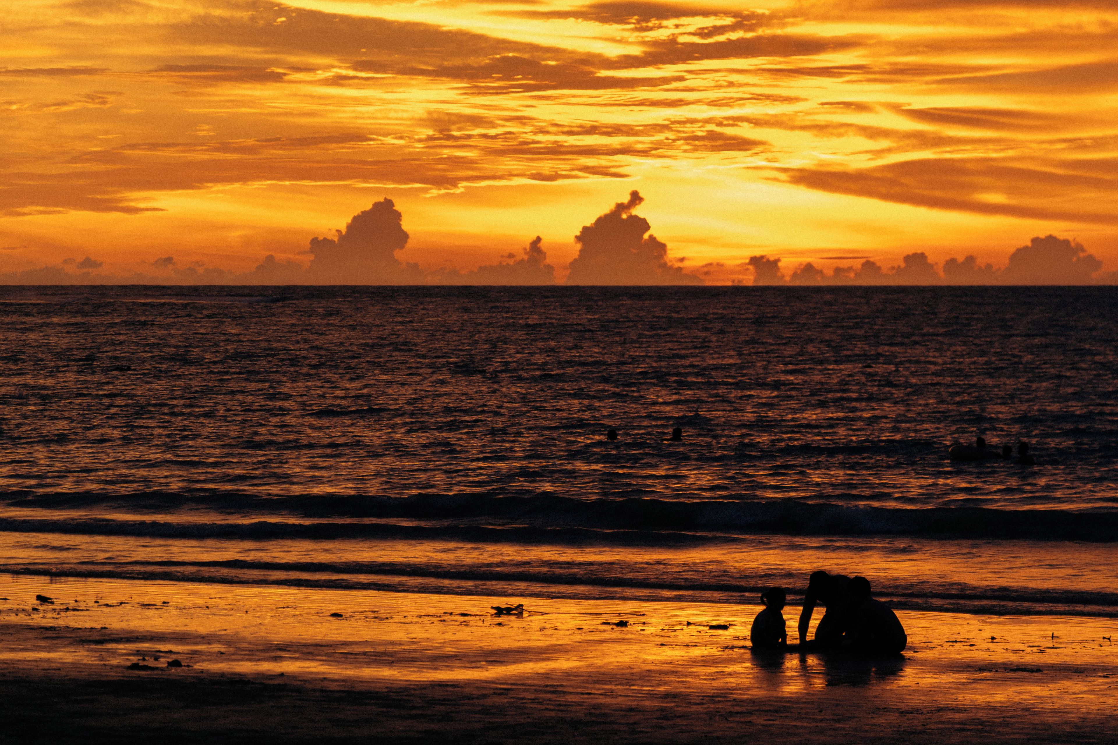 A sunset over the ocean with silhouettes of people on the beach.