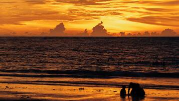 A sunset over the ocean with silhouettes of people on the beach.