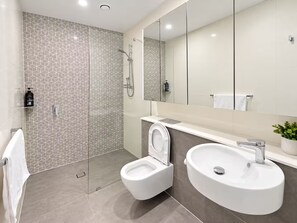 A modern bathroom with a glass-enclosed shower, a toilet, and a sink. - 3-bedroom apartment in Mascot with free parking & gym pool for relaxing stays (Mascot)