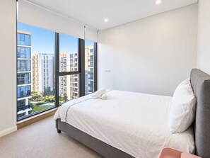 Une chambre moderne avec une grande fenêtre, un lit et une vue sur des immeubles de grande hauteur.