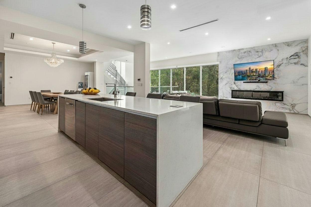 A modern kitchen with a central island, dining area, and a living space with a sofa and TV.