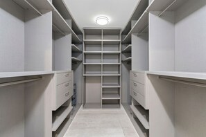 Ein begehbarer Kleiderschrank mit mehreren Regalen und Schubladen, einem hellen Boden und einer Deckenleuchte.