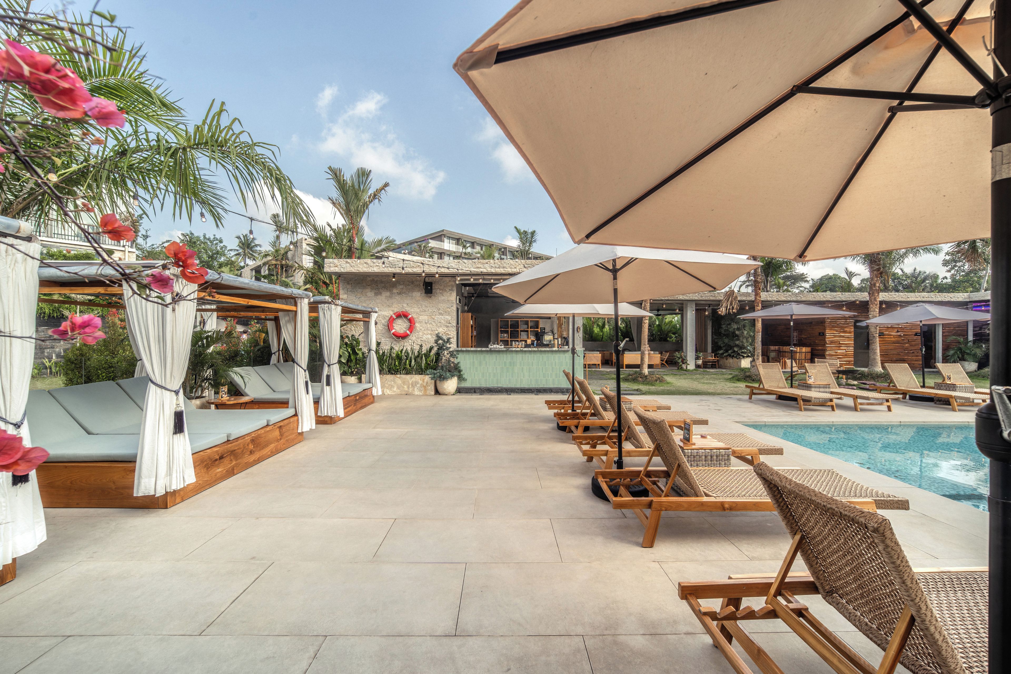 Un área junto a la piscina con sillones de descanso, sombrillas y un bar.