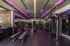 Un gimnasio con equipo de levantamiento de pesas, bancos y un espejo grande.