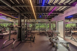 Un gimnasio con diversos equipos de ejercicio, ventanas amplias y un techo alto con vigas a la vista.