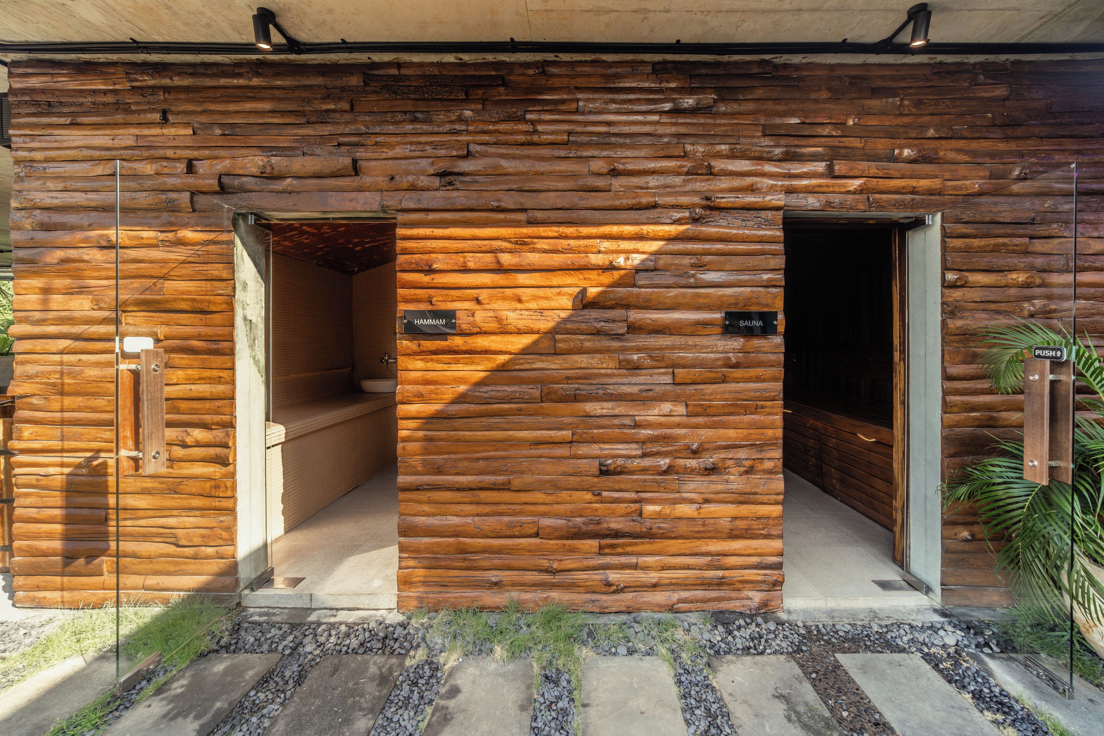 Una cabaña de troncos con dos puertas de madera que dicen 'HAMMAM' y 'SAUNA'.