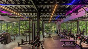 Un gimnasio con diverso equipo de ejercicio, ventanas amplias y un techo con vigas y luces a la vista.