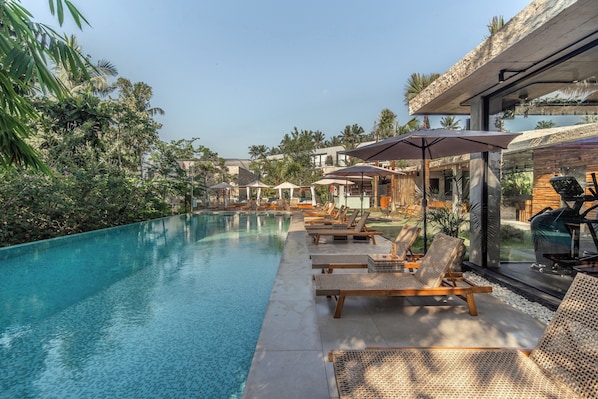 A poolside area with lounge chairs and umbrellas, surrounded by greenery and a modern building. - Saneca Resort Ubud (Ubud)