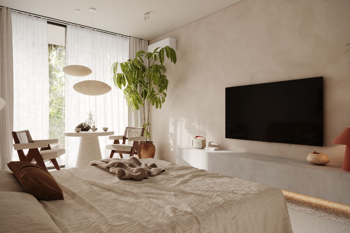Un dormitorio moderno con una cama grande, un televisor montado en la pared, una planta en maceta y una pequeña mesa con sillas.
