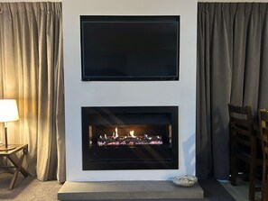 Ein Kamin mit einem Fernseher darüber, Vorhänge an beiden Seiten und eine Lampe links.