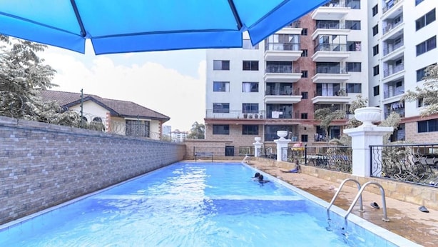 A swimming pool with a brick wall on one side and a building with balconies in the background. - Crestpark Skyline Penthouse (Nairobi)