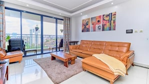 A modern living room with a leather sofa, a coffee table, and a large window overlooking a balcony. - Crestpark Skyline Penthouse (Nairobi)