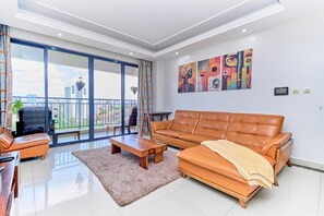 A modern living room with a leather sofa, a coffee table, and a large window overlooking a balcony. - Crestpark Skyline Penthouse (Nairobi)