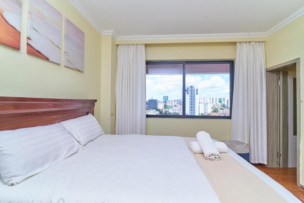Quarto de hotel com cama, janela com cortinas e vista para a cidade.