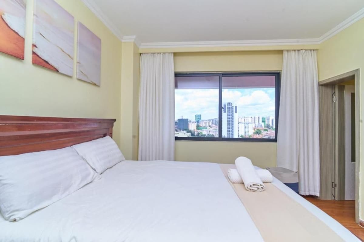 A hotel room with a bed, a window with curtains, and a city view.
