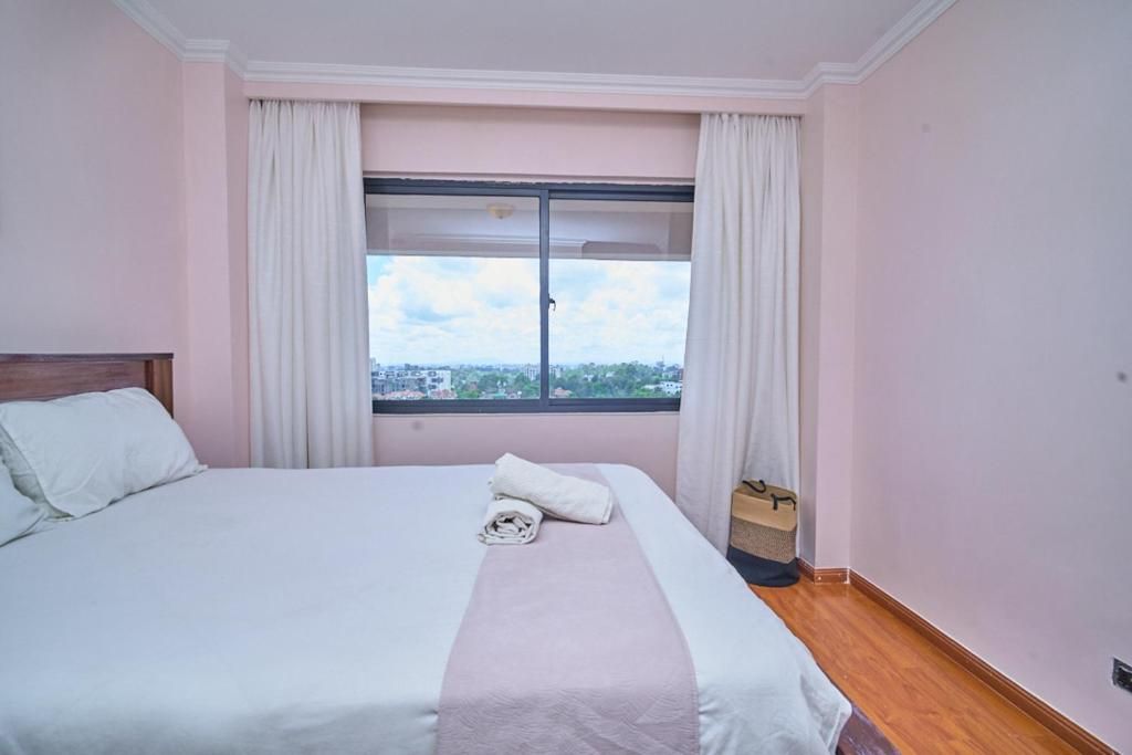 Habitación de hotel con cama, ventana con cortinas y vista a la ciudad.
