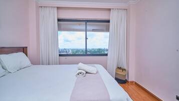 Habitación de hotel con cama, ventana con cortinas y vista a la ciudad.