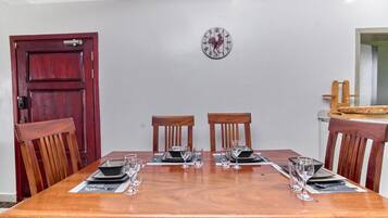 Un comedor con una mesa de madera dispuesta para cuatro personas, con dos sillas a cada lado y un reloj fijado a la pared.