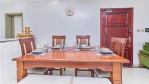 A dining area with a wooden table set for four, surrounded by chairs. A clock is mounted on the wall above the table. - Crestpark Skyline Penthouse (Nairobi)