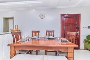 A dining area with a wooden table set for four, surrounded by chairs. A clock is mounted on the wall above the table. - Crestpark Skyline Penthouse (Nairobi)