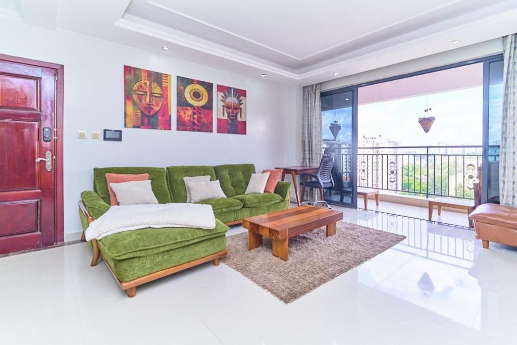 A modern living room with a green sofa set, a wooden coffee table, and a balcony with a view.