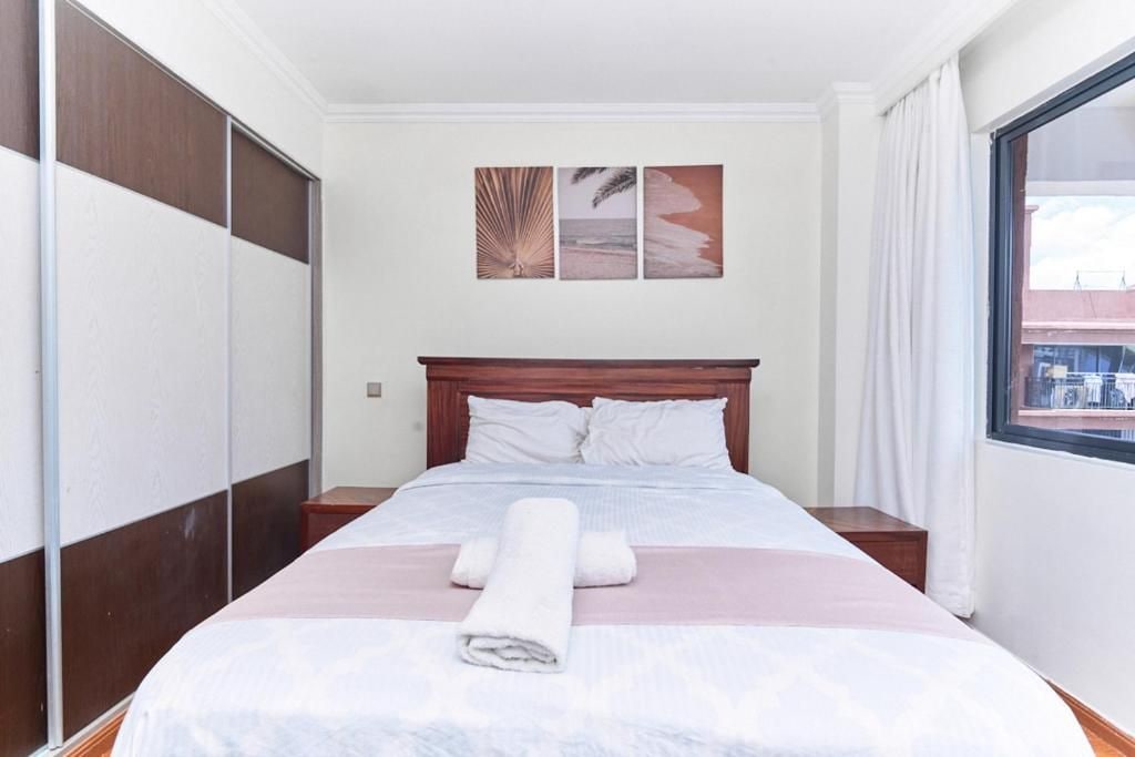 Una habitación de hotel con una cama, cabecera de madera, ventana con cortinas y una obra de arte en la pared.