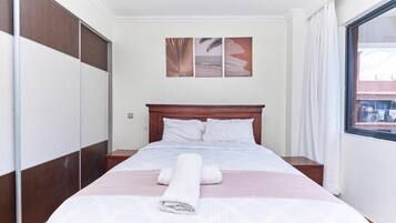 Una habitación de hotel con una cama, cabecera de madera, ventana con cortinas y una obra de arte en la pared.