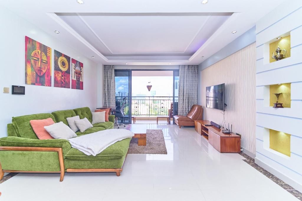 Uma sala de estar moderna com um sofá verde, uma TV de tela plana e obras de arte nas paredes.