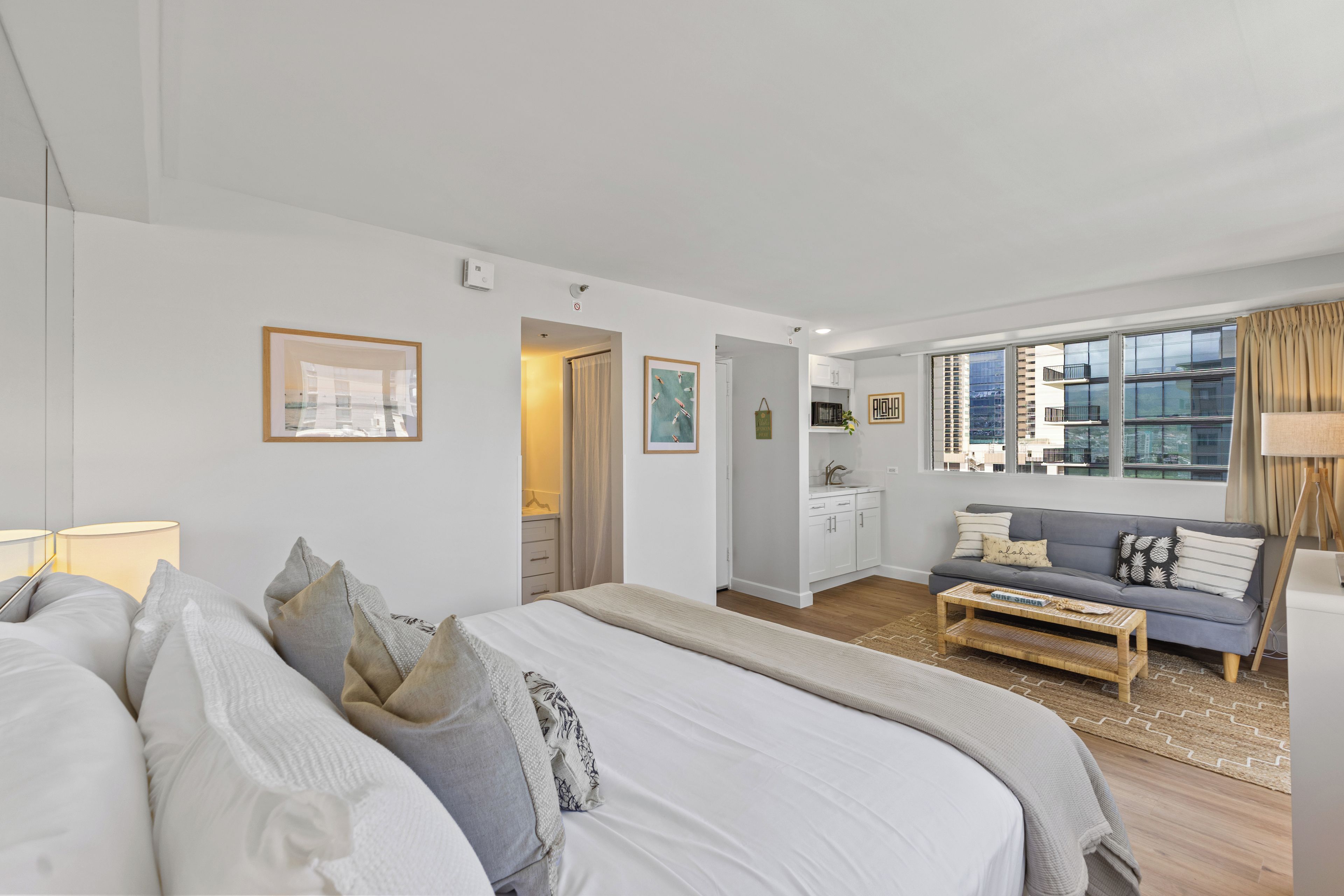 Ein modernes Hotelzimmer mit Bett, einer Sitzecke, einer kleinen Küchenzeile und Blick auf die Stadt.