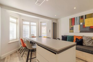 A modern kitchen with a central island, bar stools, and a seating area with a sofa and cushions. - Bright 2BR Oxford Flat | Free Parking & City Access (Oxfordshire)