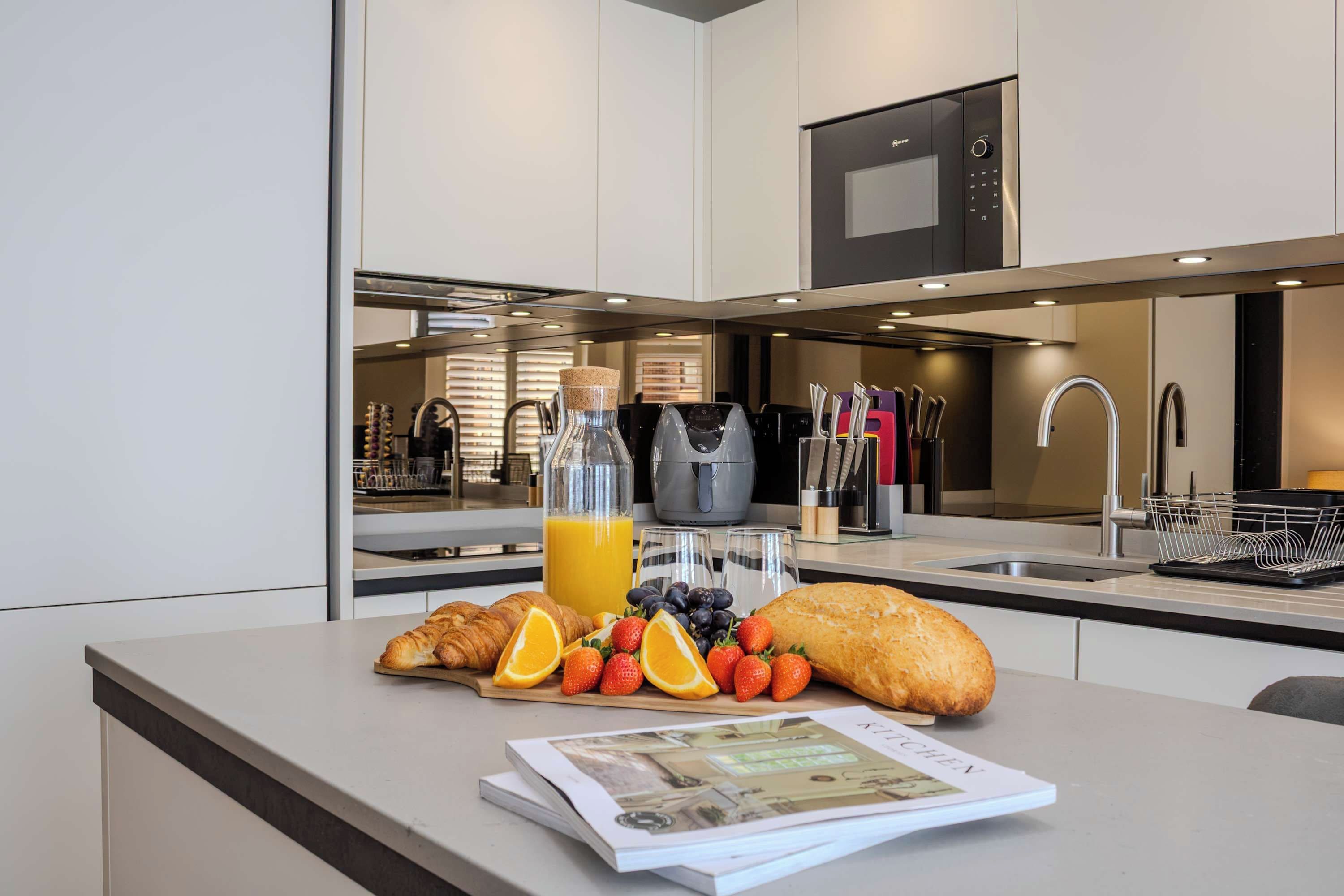 Eine moderne Küche mit Frühstücksangebot, darunter Croissants, Früchte und eine Saftflasche.