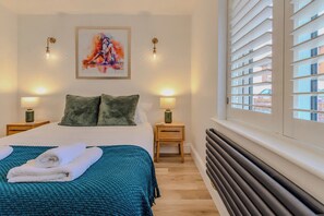 Ein Hotelzimmer mit einem Bett, zwei Nachttischen, einer Heizung und einem Fenster mit Jalousien.