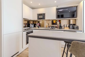 A modern kitchen with a central island, built-in appliances, and a flat-screen TV above the counter. - Bright 2BR Oxford Flat | Free Parking & City Access (Oxfordshire)
