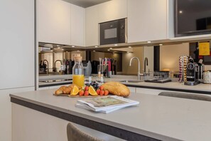 Eine moderne Küche mit Frühstücksangebot, darunter Croissants, Obst und eine Kaffeemaschine.