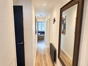 A hallway with a door, a radiator, and a bed in the distance. - Bright 2BR Oxford Flat | Free Parking & City Access (Oxfordshire)