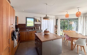 A modern kitchen with wooden cabinets, a central island, and a dining area with a table and chairs. - Maison proche Aix-en-Provence (Le Tholonet)