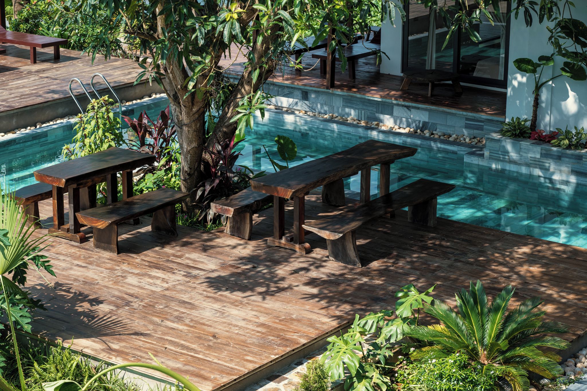 A poolside area with wooden benches and a tree.