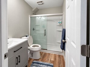 Un baño moderno con cabina de ducha de vidrio, un inodoro blanco y un lavabo con mueble.
