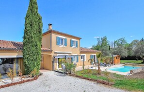 Uma casa de dois andares com piscina, varanda coberta e uma imponente árvore cipreste.